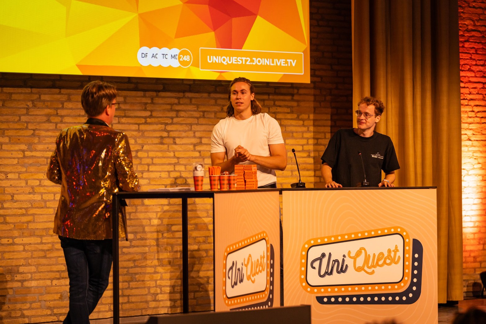 Jerre Maas in gouden glitterjasje met de kandidaten aan de UniQuest-desk
