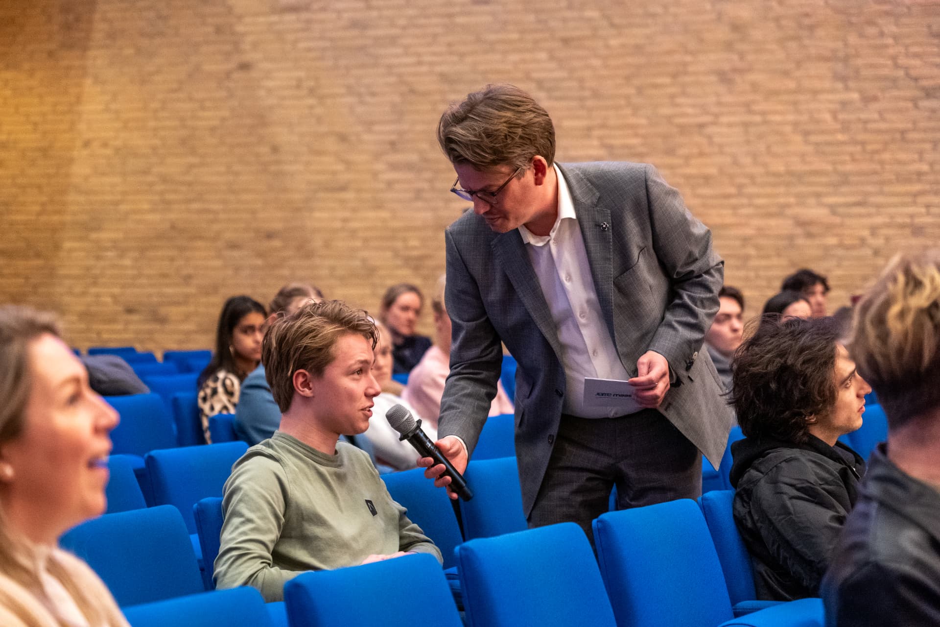 Jerre Maas houdt de microfoon voor een deelnemer in de zaal