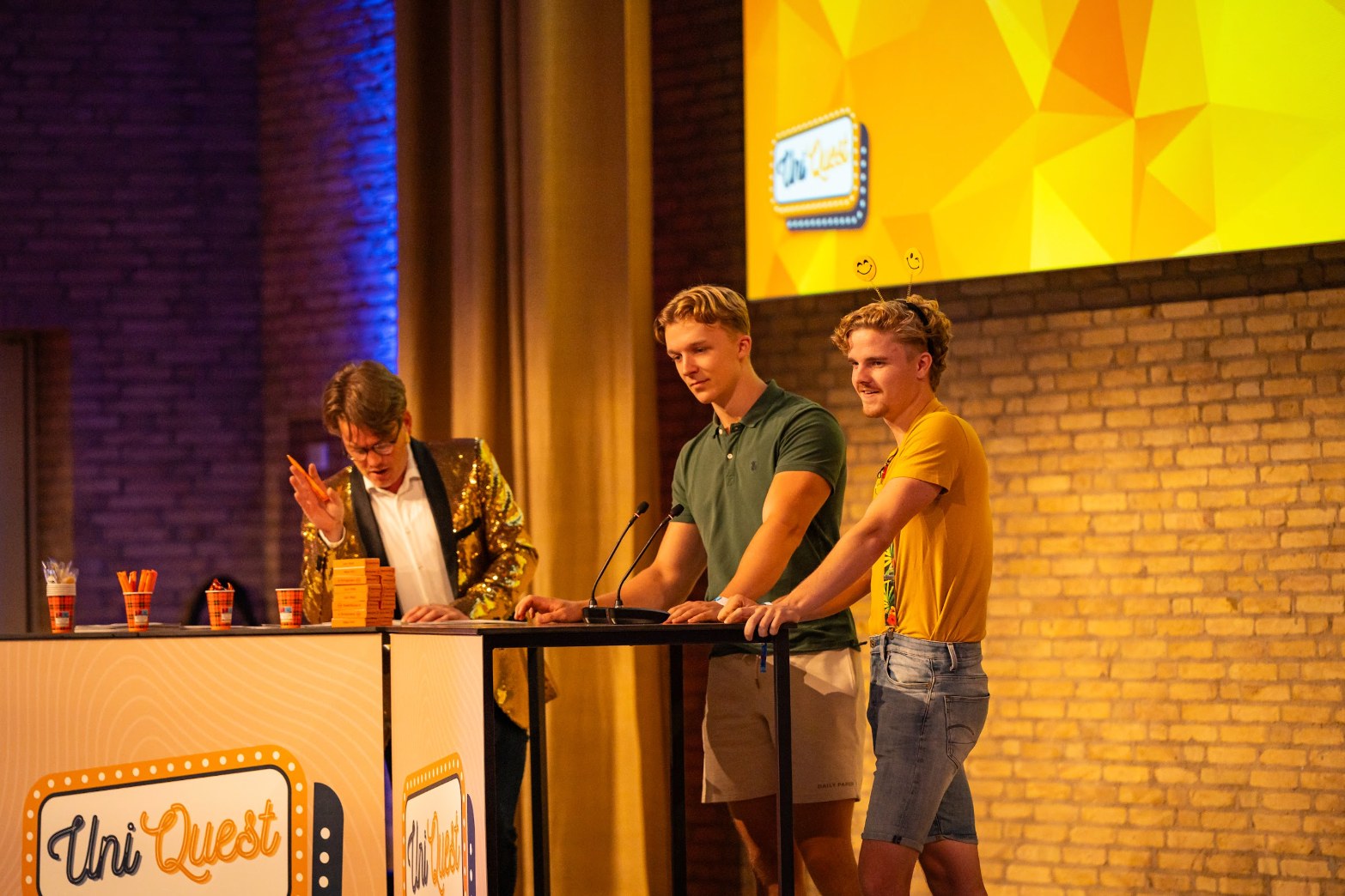 Jerre Maas leest een vraag voor terwijl twee kandidaten aan de UniQuest-desk meekijken